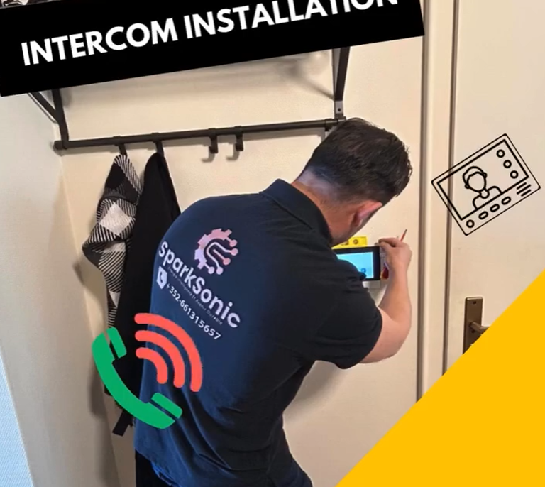 Sparksonic technician installing a wall-mounted intercom system inside a home, equipped with tools and a screen tester.