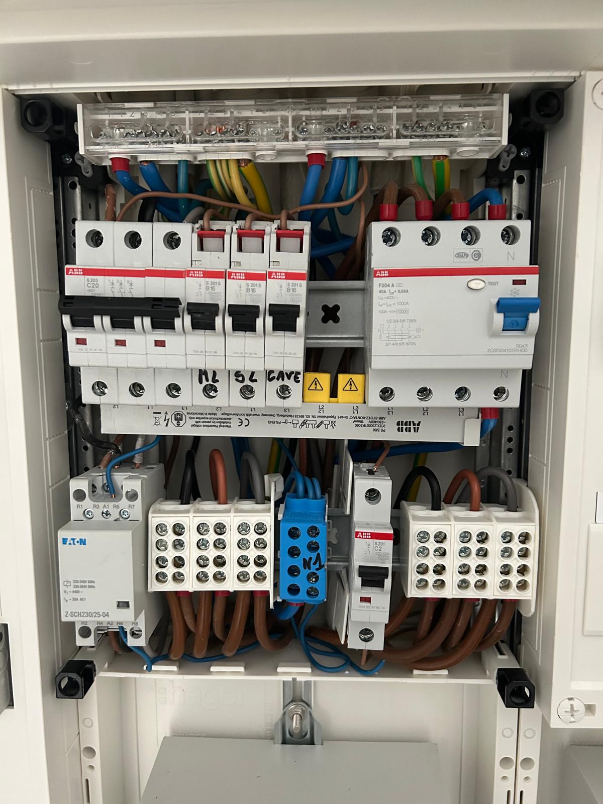 Electrical distribution board with multiple circuit breakers, relays, and wiring connections neatly installed in a metal panel box.